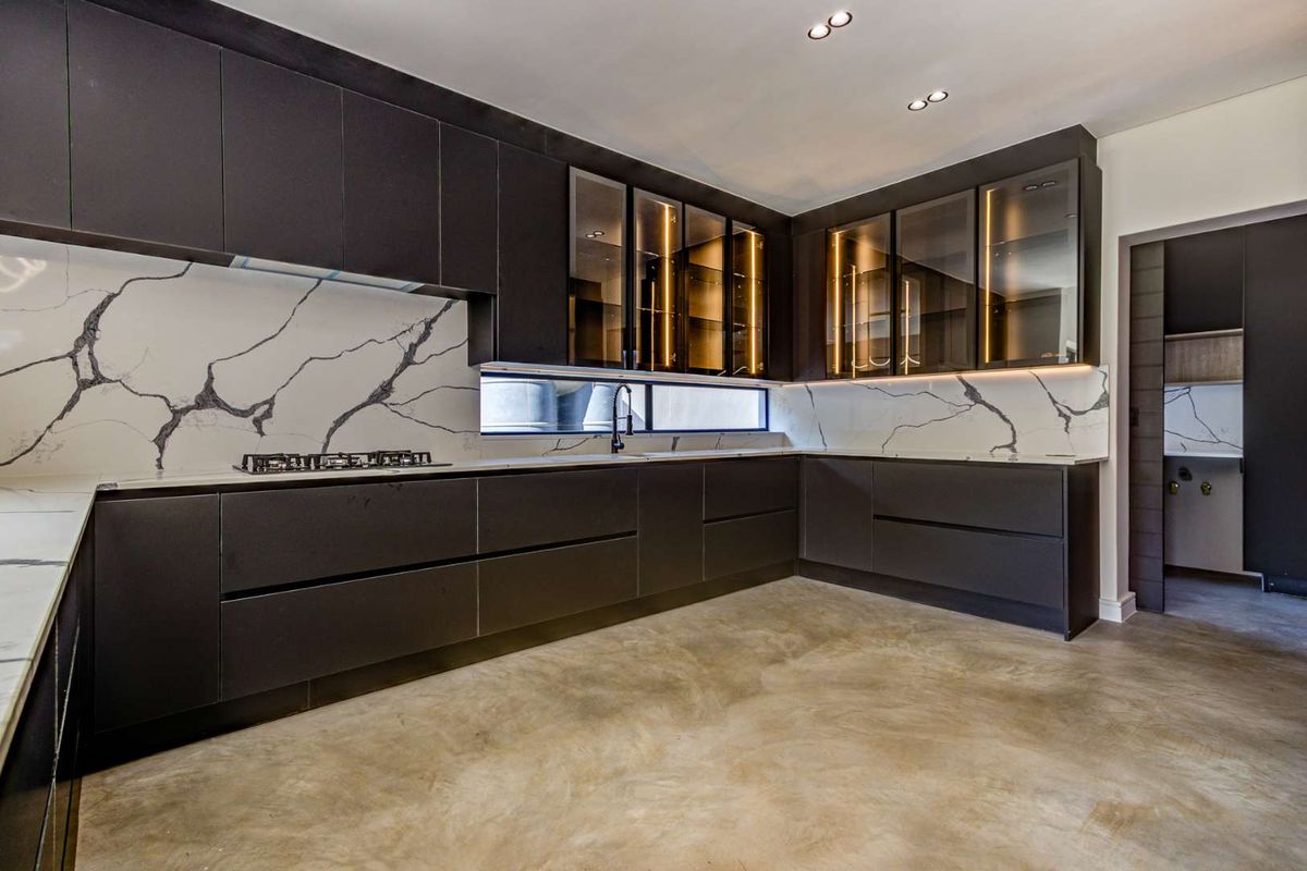 Modern kitchen featuring sleek dark cabinetry, marble-look stone splashbacks, integrated lighting, and a gas hob, set against a polished concrete floor.