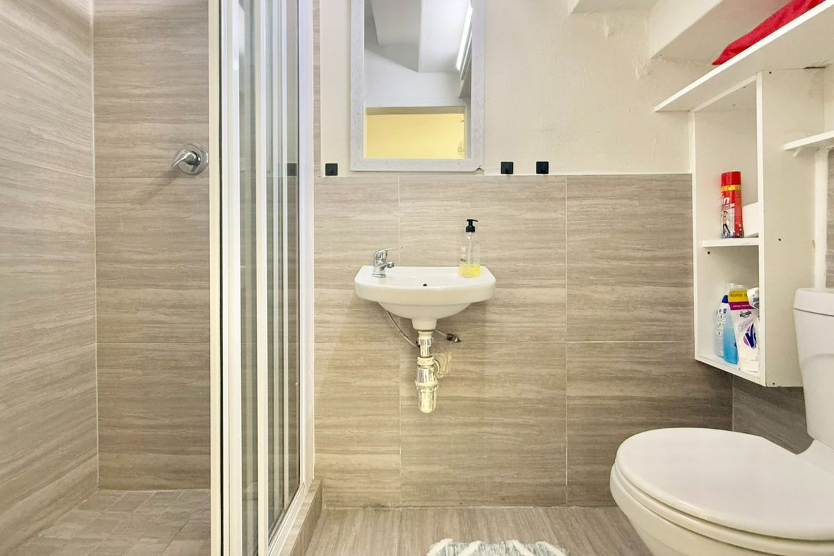 Compact bathroom featuring a shower enclosure, wall-mounted basin, toilet, and neutral wood-look wall tiling with built-in shelving.