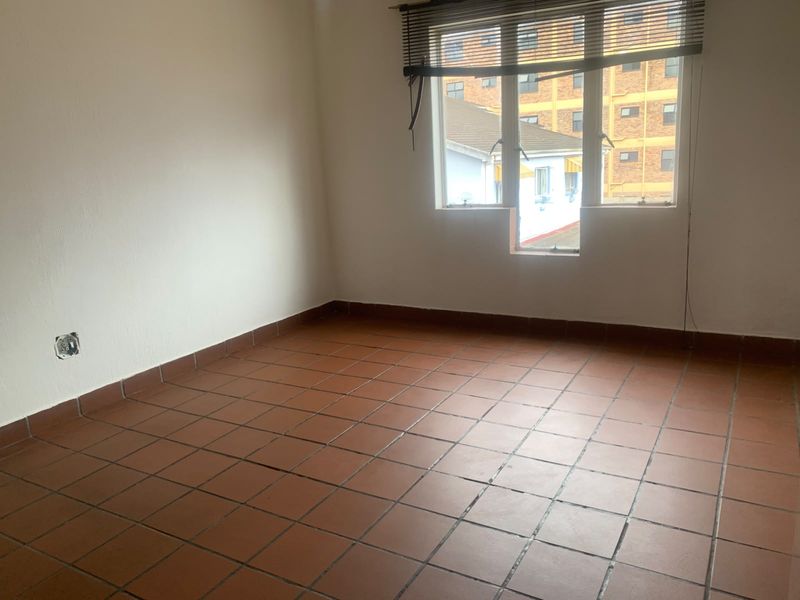 An empty bedroom featuring terracotta floor tiles and a window with venetian blinds, requiring minor repairs to electrical fittings.