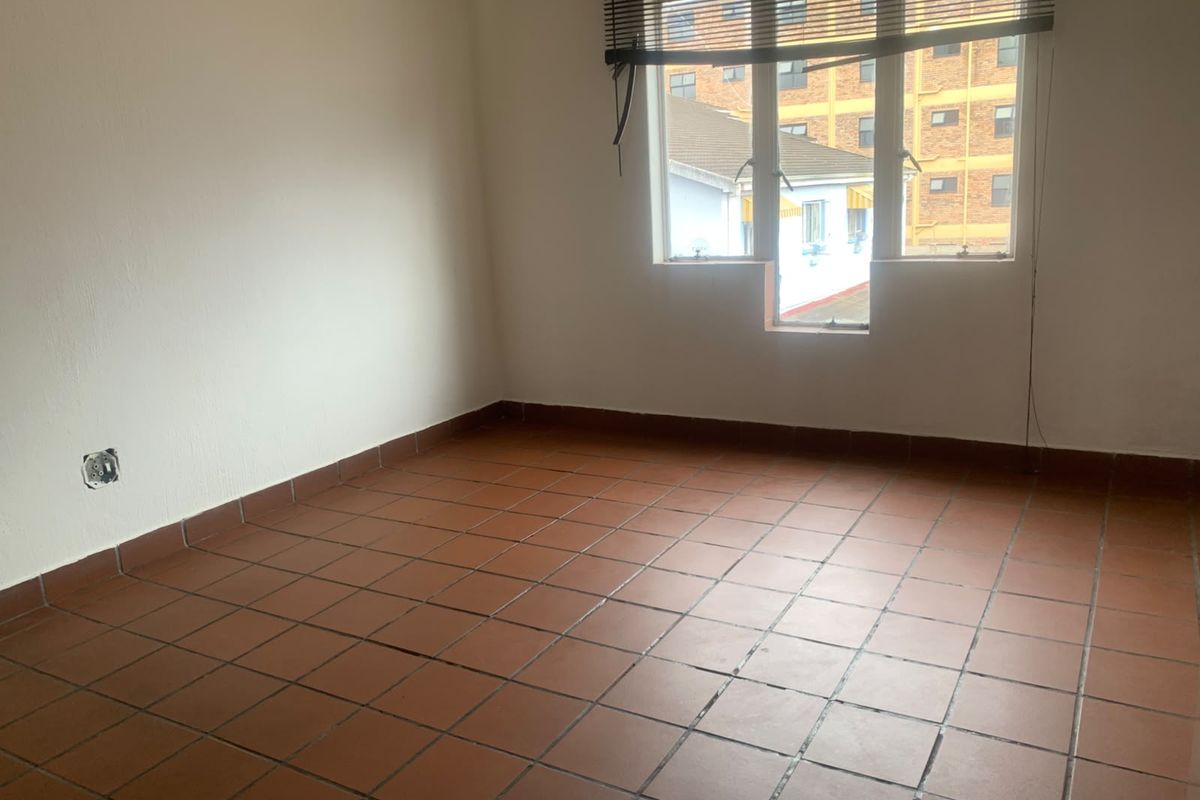 An empty bedroom featuring terracotta floor tiles and a window with venetian blinds, requiring minor repairs to electrical fittings.