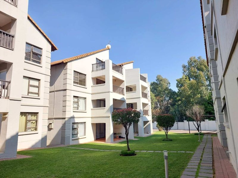 Exterior view of a multi-story apartment complex featuring private balconies, well-maintained green lawns, and paved walkways within a secure residential estate.