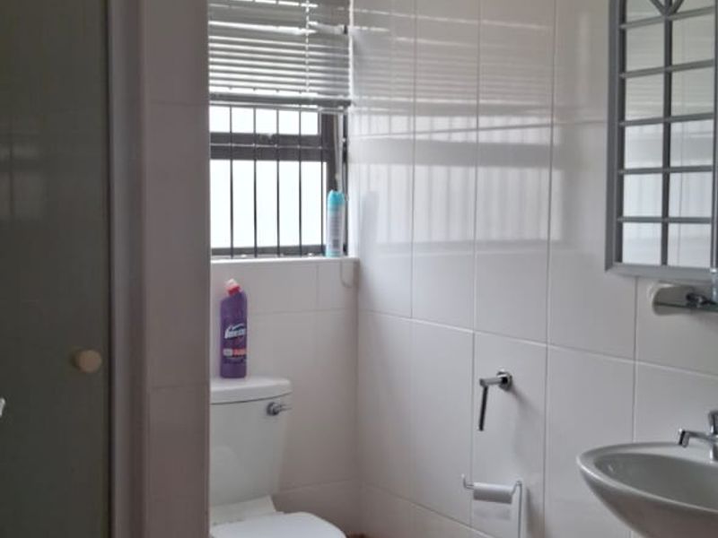 A functional bathroom featuring a shower enclosure, pedestal washbasin, and toilet, finished with neutral wall and floor tiles.
