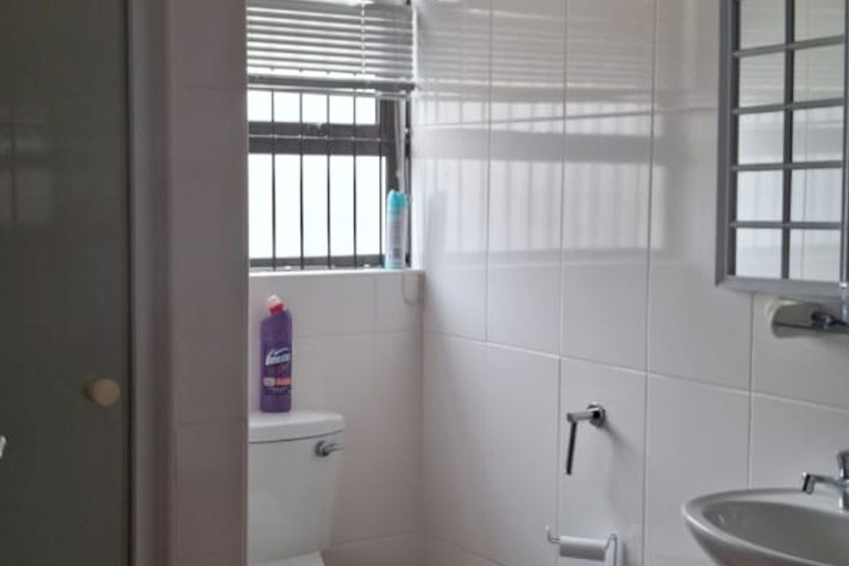 A functional bathroom featuring a shower enclosure, pedestal washbasin, and toilet, finished with neutral wall and floor tiles.