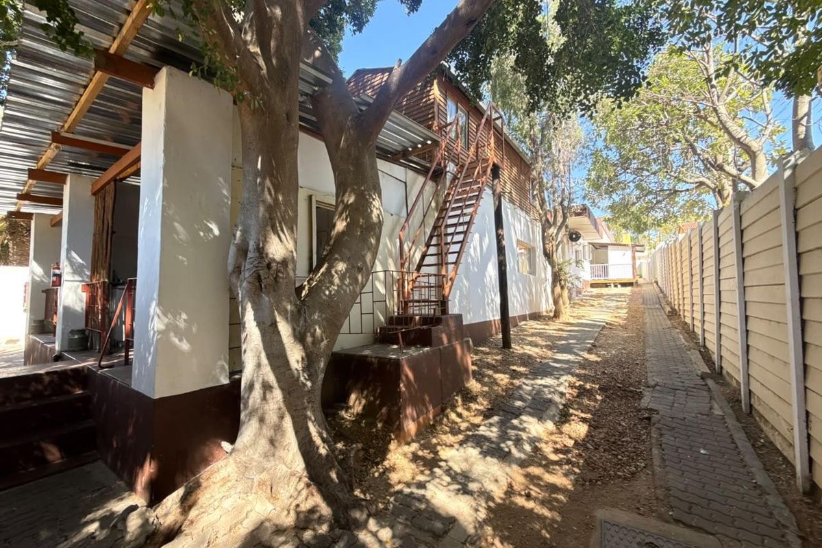 Rear exterior view of the property featuring a paved walkway, mature trees, and an external metal staircase leading to the upper level.
