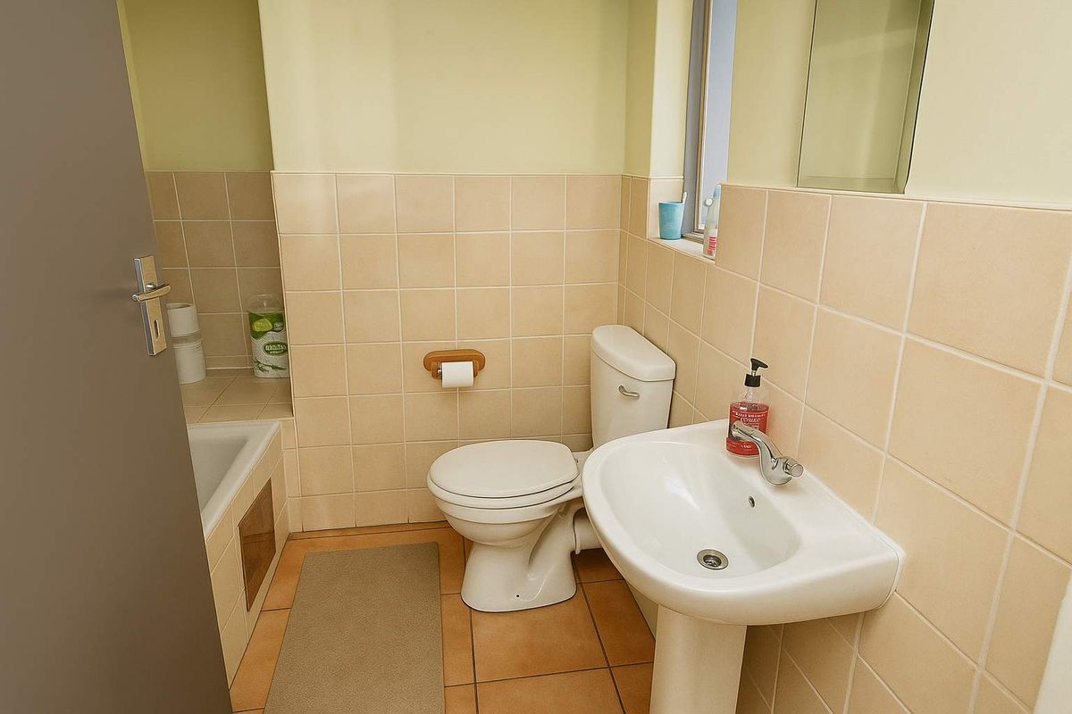 A functional bathroom featuring a pedestal sink, toilet, and a tiled bathtub surround with neutral wall tiling.