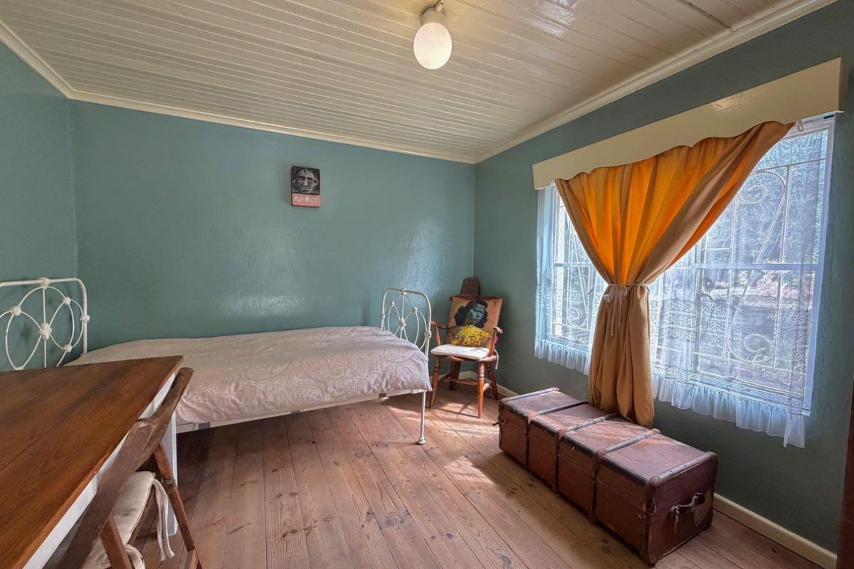 A bedroom featuring original timber flooring, a tongue and groove ceiling, and a window fitted with security bars.