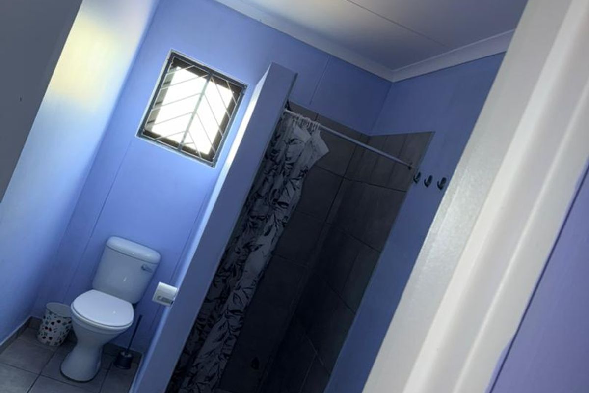 A functional bathroom featuring a tiled floor, a toilet, a shower enclosure with a curtain, and a wall-mounted basin.
