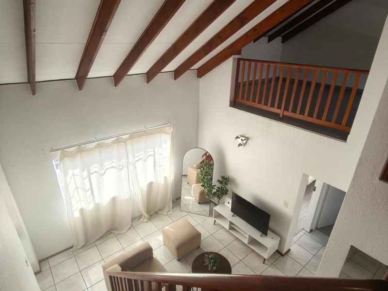 Spacious double-volume living area featuring exposed timber ceiling beams, a mezzanine level with wooden balustrades, and tiled flooring throughout.