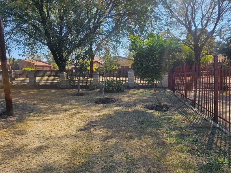 A spacious garden area featuring established trees, perimeter fencing with masonry pillars, and a metal gate, offering a private outdoor space.