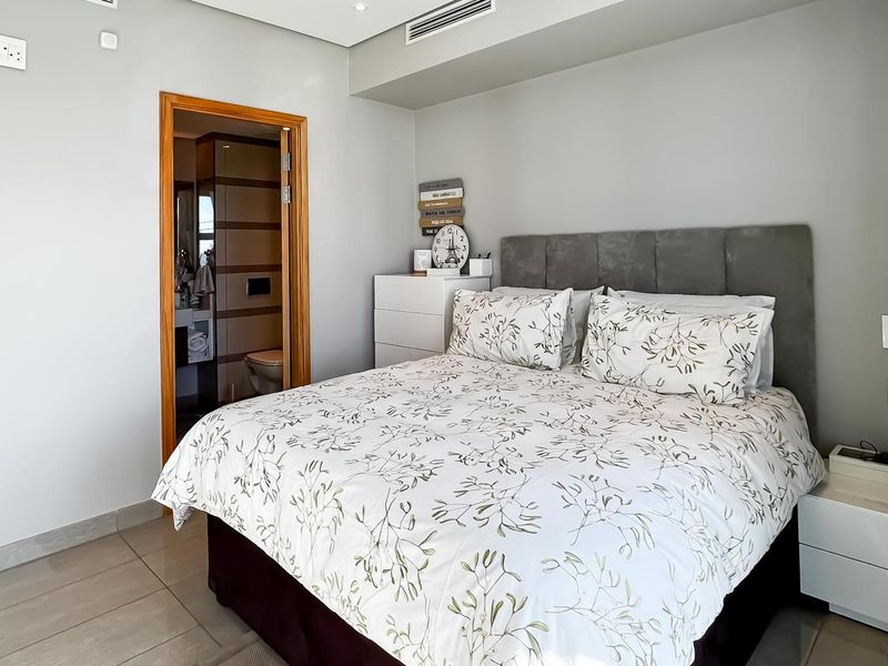 A well-maintained bedroom featuring neutral wall finishes, tiled flooring, recessed ceiling lighting, and an en-suite bathroom access.