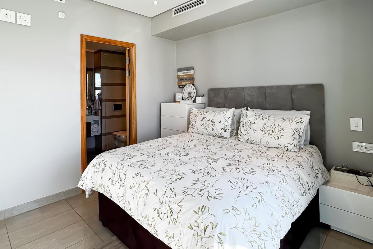 A well-maintained bedroom featuring neutral wall finishes, tiled flooring, recessed ceiling lighting, and an en-suite bathroom access.