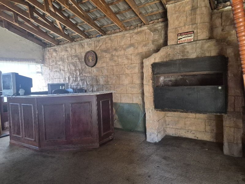 Rustic bar area featuring a built-in counter, stone fireplace, and exposed timber roof trusses, offering significant potential for renovation and modernization.
