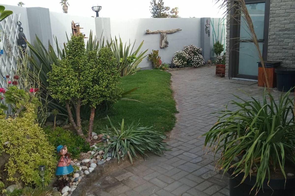 A well-maintained rear garden area featuring paved walkways, landscaped garden beds, and a brick-finished exterior wall with integrated lighting.