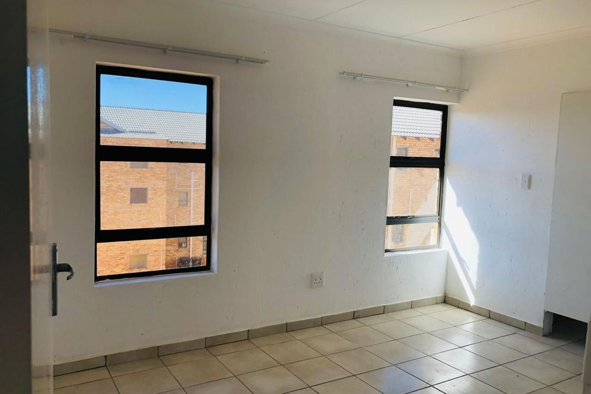 A bright, empty bedroom featuring tiled flooring, large windows with metal frames, and built-in storage.