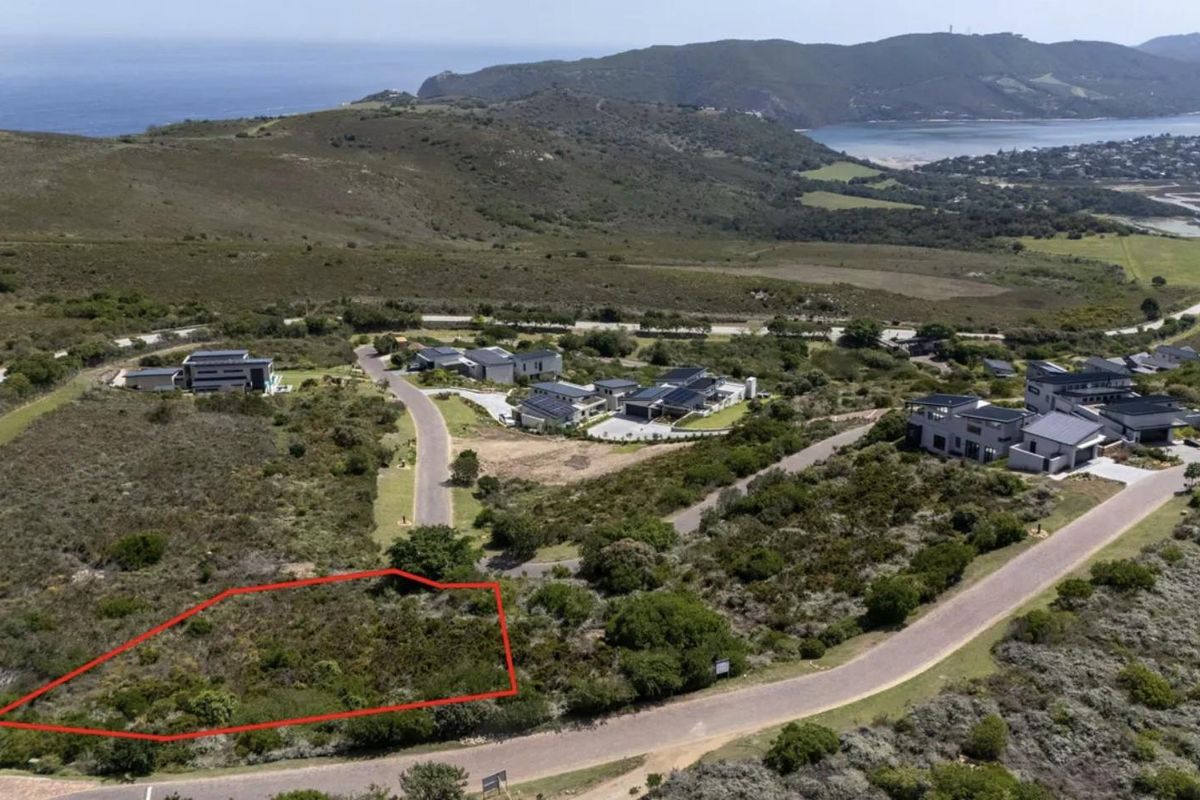 Aerial view of a vacant residential plot in a coastal estate, featuring natural vegetation and established road access.