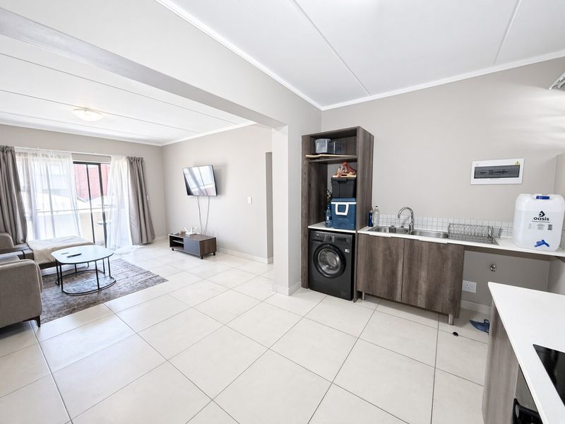An open-plan living area featuring tiled flooring, a compact kitchenette with built-in cabinetry, and a sliding door leading to a balcony.