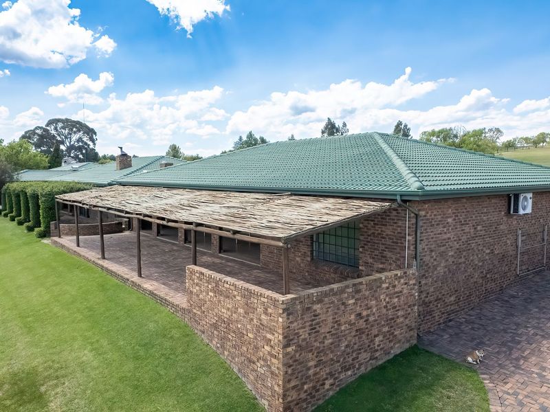 Rear view of a brick house featuring a large covered patio with a timber pergola, tiled roof, and expansive surrounding lawn.