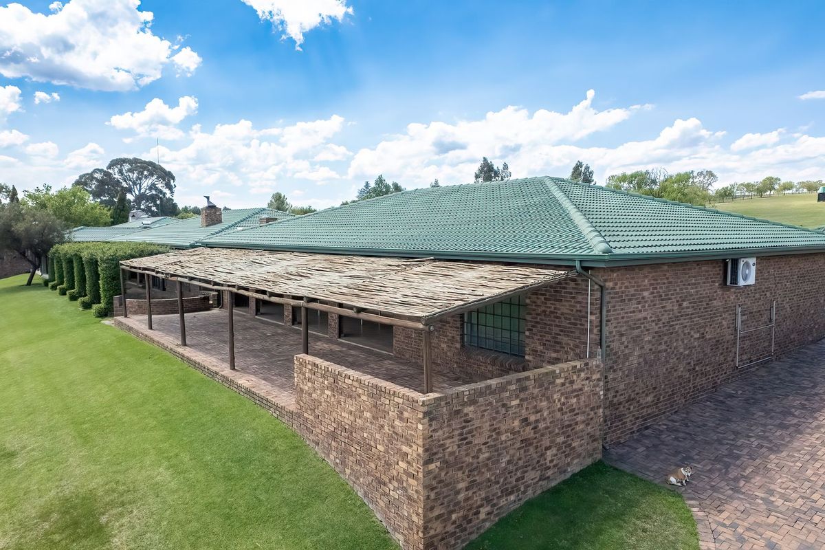 Rear view of a brick house featuring a large covered patio with a timber pergola, tiled roof, and expansive surrounding lawn.