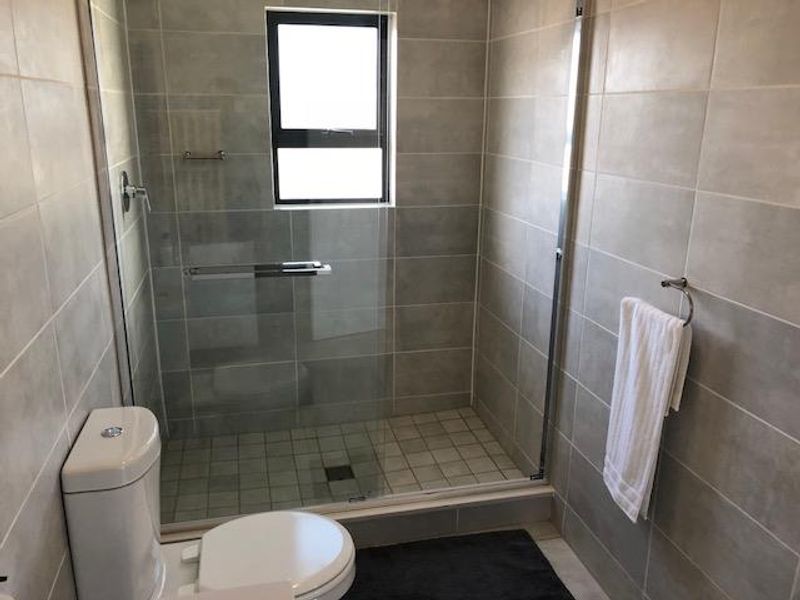 Modern bathroom featuring a glass-enclosed shower, neutral ceramic wall and floor tiles, and a standard toilet.