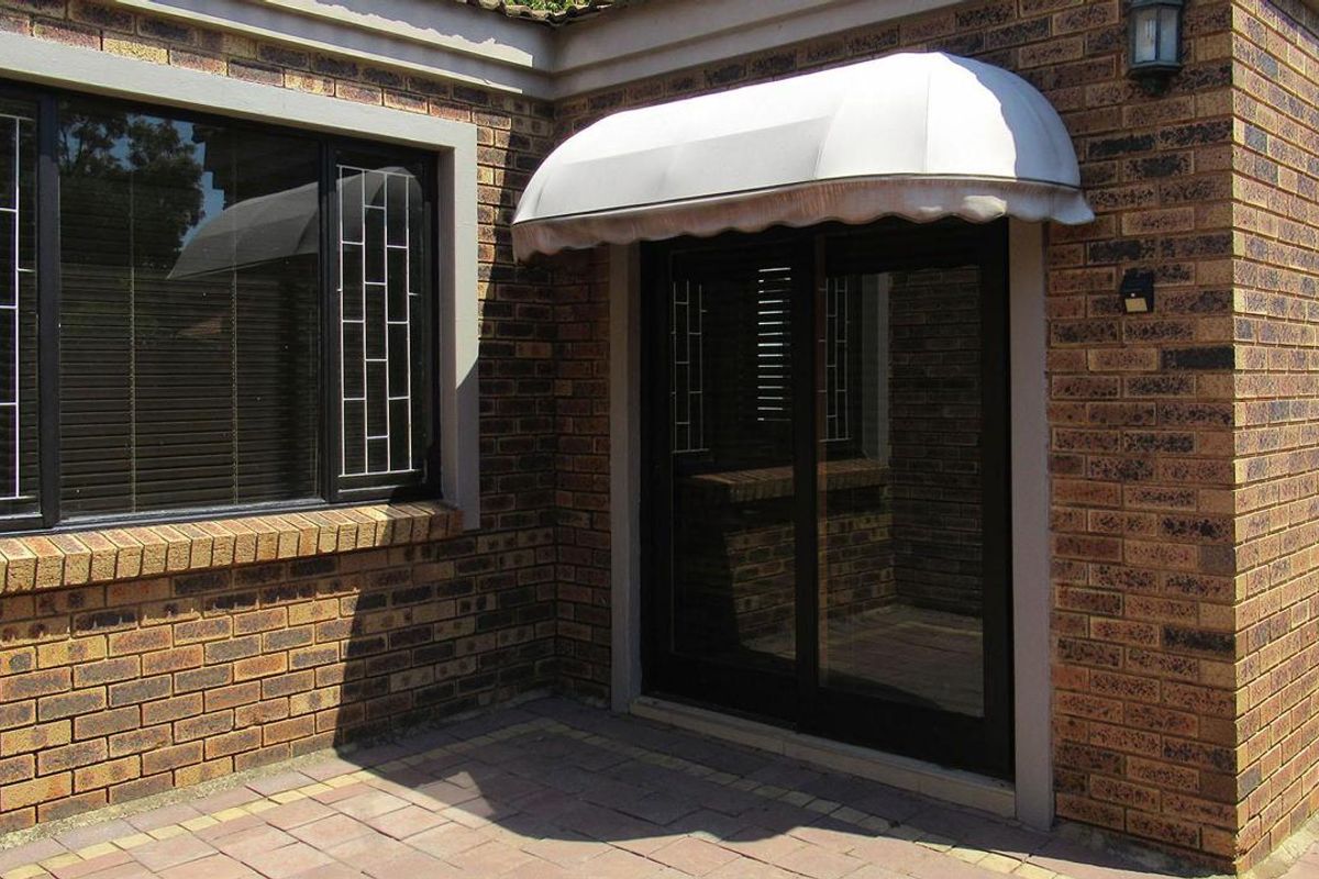 Exterior view of a brick facade featuring a sliding glass door with a protective awning and adjacent window with security bars.