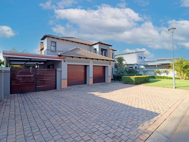 Front view of a modern double-story house featuring a paved driveway, double garage, and an attached carport with a well-maintained garden.
