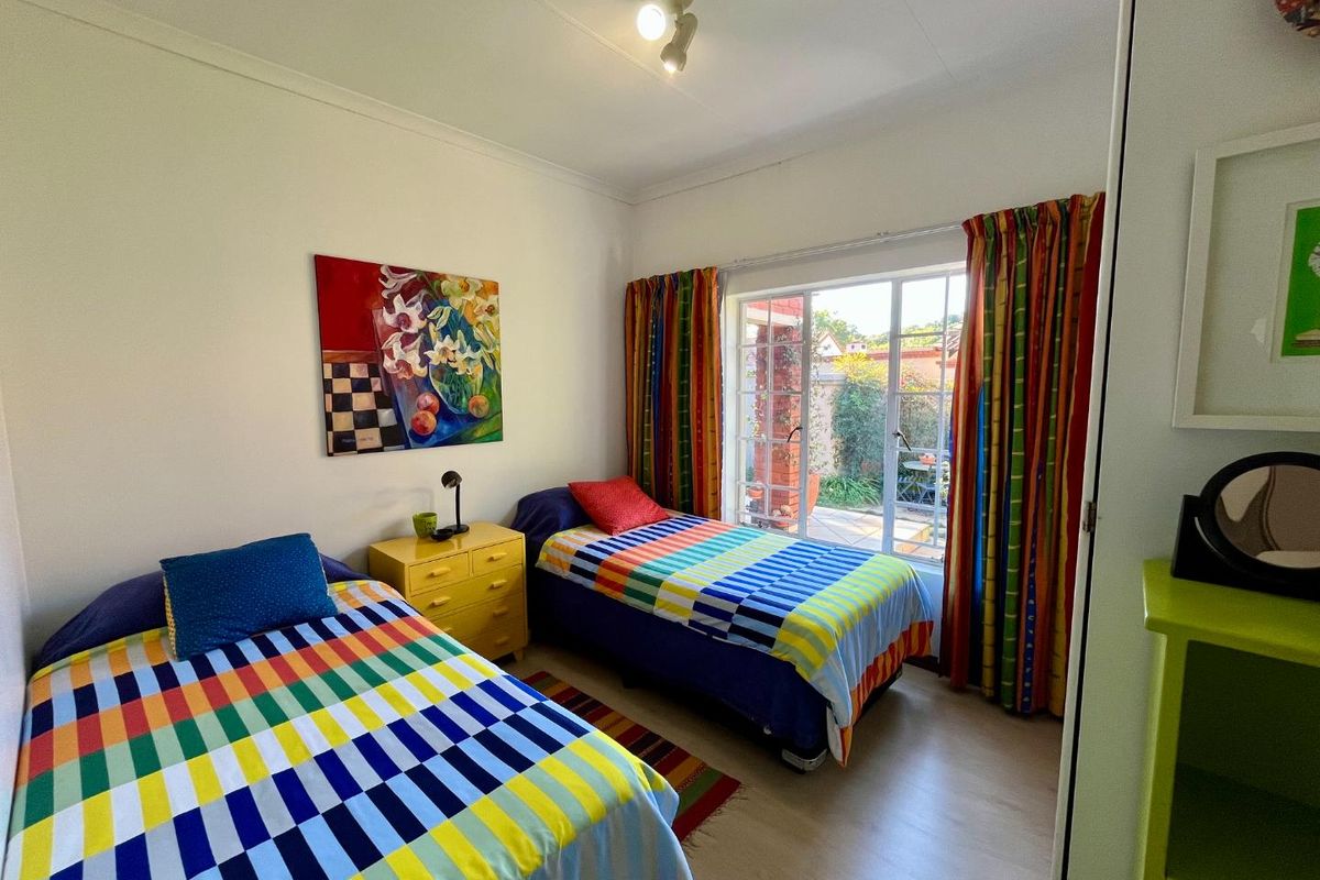 A bright bedroom featuring laminate flooring, built-in cupboard space, and a large window providing natural light and access to the outdoor area.