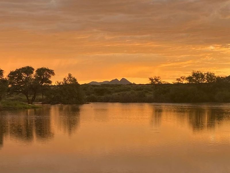 A scenic view of a tranquil dam on the agricultural property, featuring natural landscape and sunset reflections.