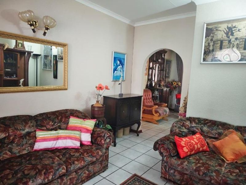 A living room featuring tiled flooring, a decorative archway leading to an adjacent space, and wall-mounted lighting fixtures.