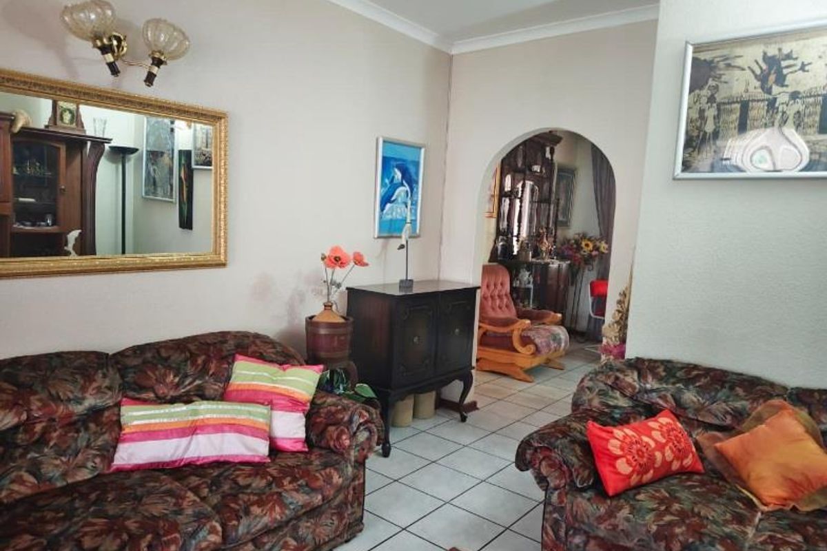 A living room featuring tiled flooring, a decorative archway leading to an adjacent space, and wall-mounted lighting fixtures.
