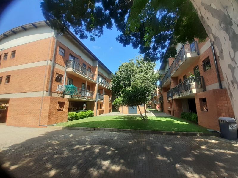 A view of the apartment complex exterior featuring brick facades, private balconies, a central lawn area, and paved driveway access.