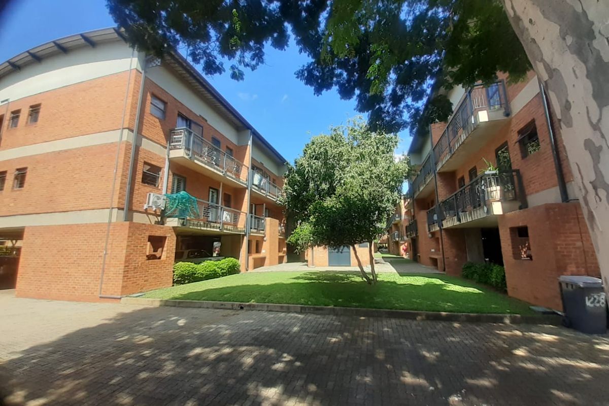 A view of the apartment complex exterior featuring brick facades, private balconies, a central lawn area, and paved driveway access.