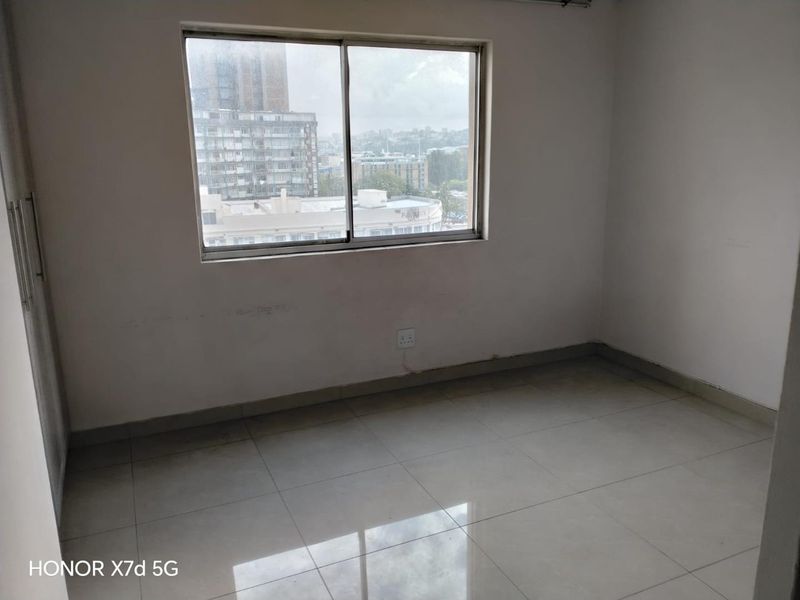 An empty bedroom featuring tiled flooring, a built-in cupboard, and a window with an urban view.