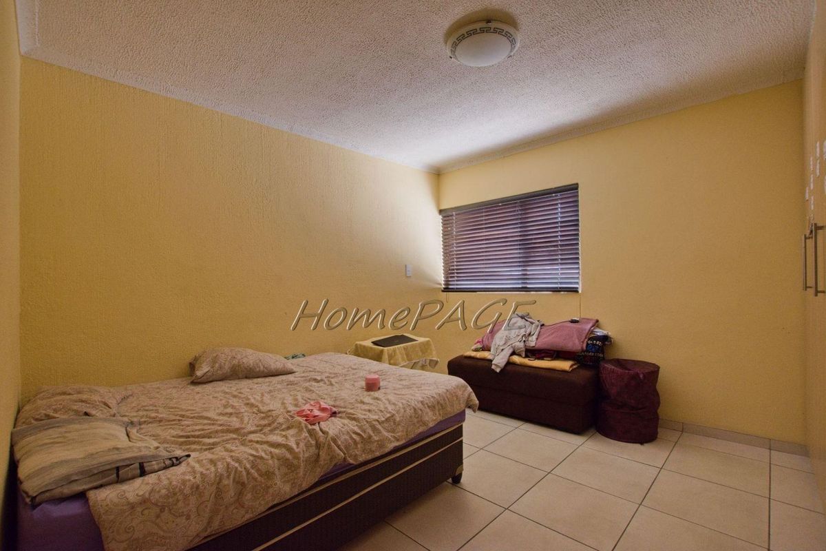 A bedroom featuring tiled flooring, a window with fitted blinds, and a central ceiling light fixture.