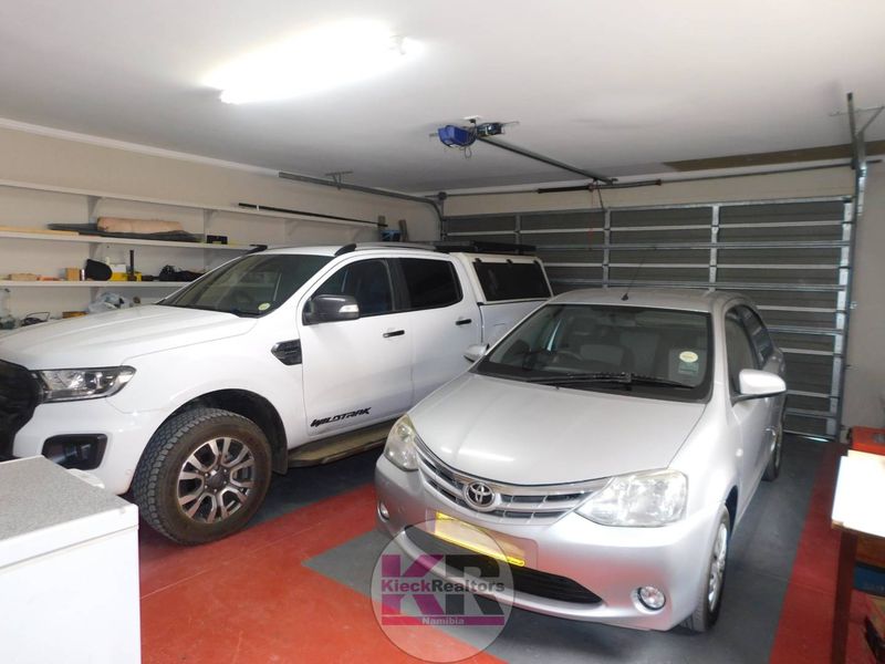 Spacious double garage featuring a sectional door, built-in shelving for storage, and overhead fluorescent lighting.