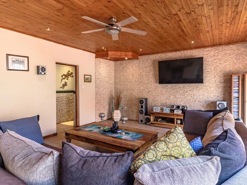 A cozy living room featuring a warm timber tongue and groove ceiling, stone-clad feature wall, and recessed lighting.