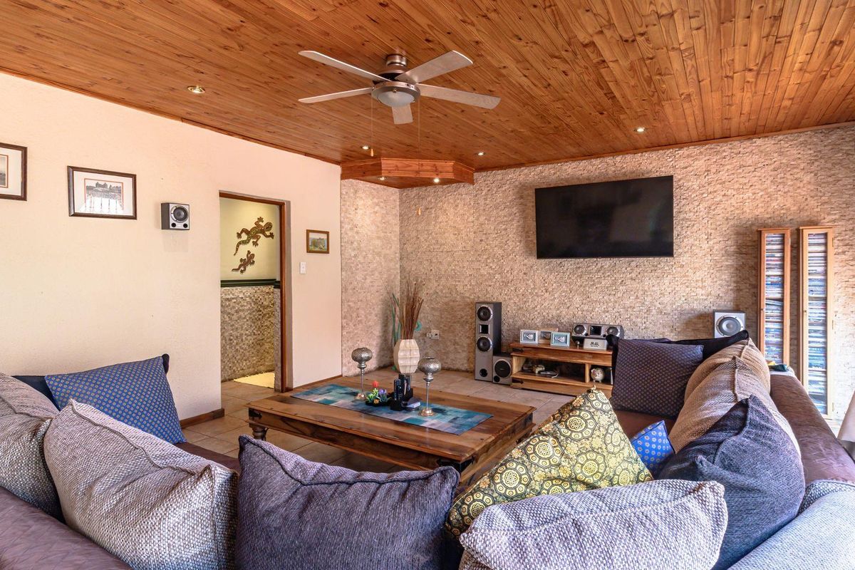 A cozy living room featuring a warm timber tongue and groove ceiling, stone-clad feature wall, and recessed lighting.