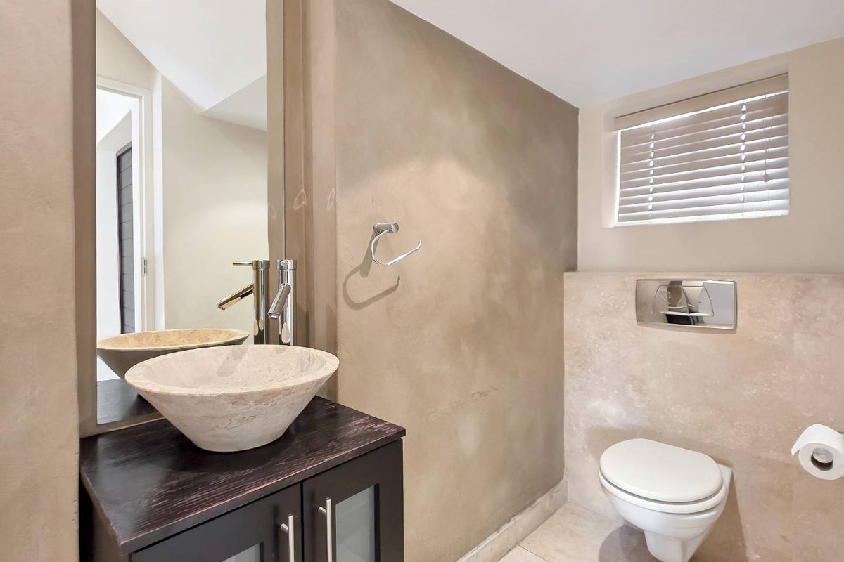 Modern guest bathroom featuring a stone vessel sink, dark wood vanity, wall-mounted toilet, and neutral textured wall finishes.