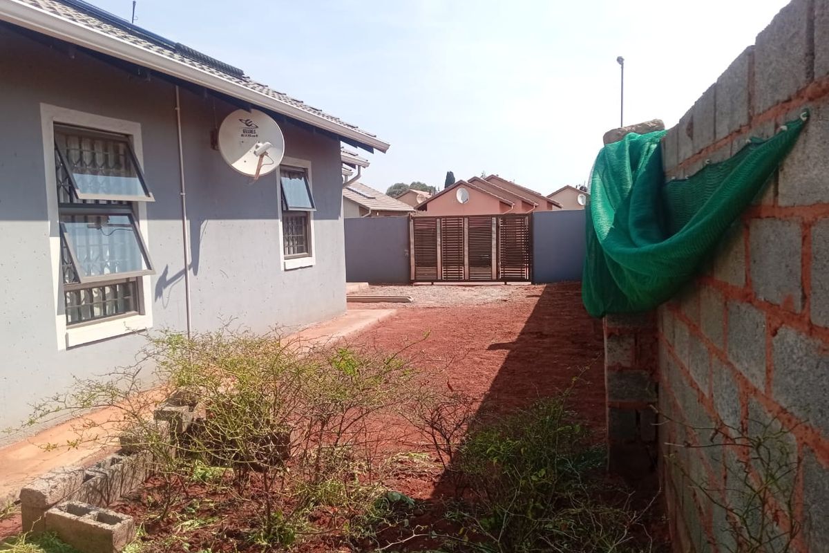 Rear exterior view of the property featuring a side yard with unlandscaped ground, boundary wall, and metal gate access.