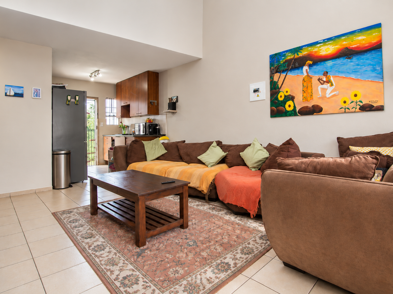 Open-plan living area featuring high vaulted ceilings, tiled flooring, and a functional kitchen space with wood-finish cabinetry.