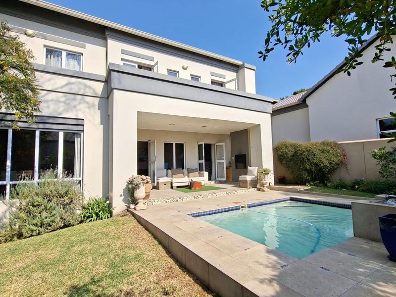 Rear view of the property featuring a covered patio, a swimming pool with tiled surround, and a balcony overlooking the garden area.