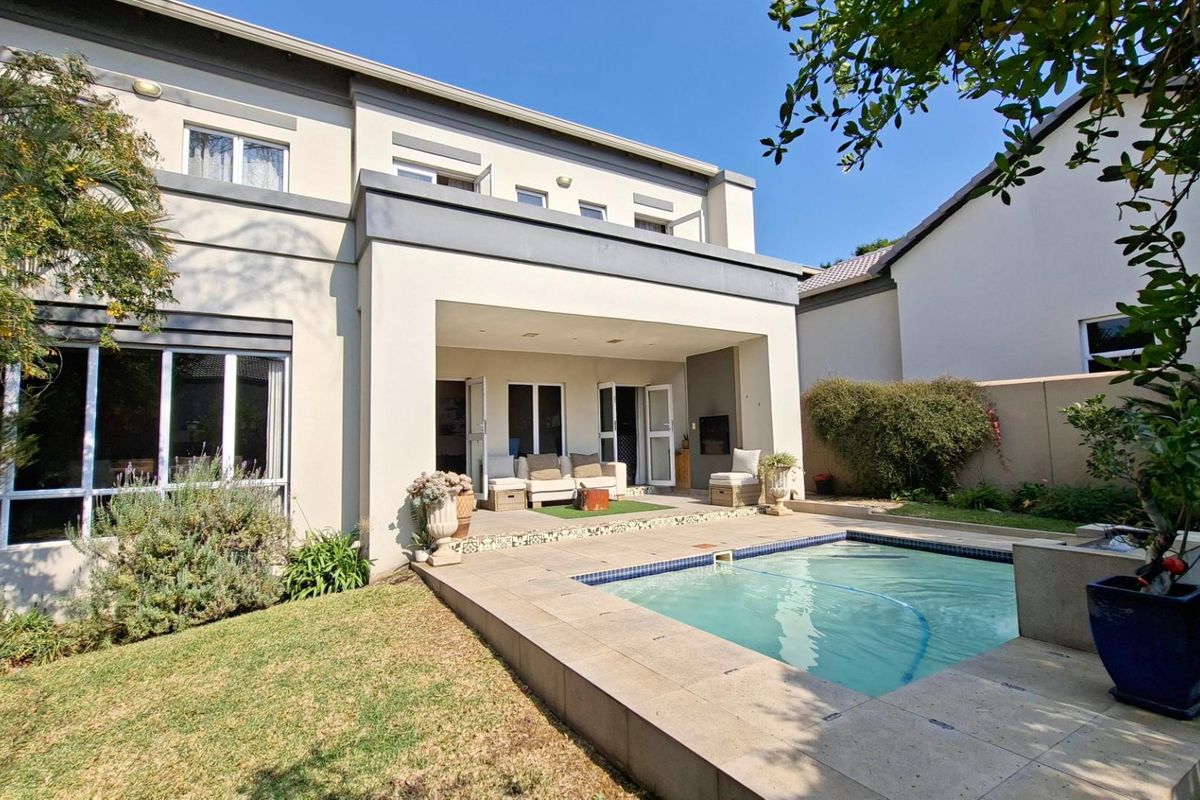 Rear view of the property featuring a covered patio, a swimming pool with tiled surround, and a balcony overlooking the garden area.
