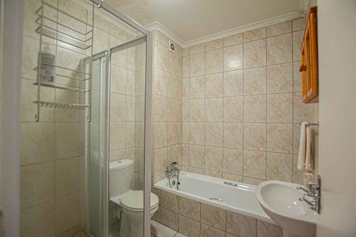 A functional bathroom featuring a shower enclosure, bathtub, pedestal basin, and toilet with neutral tiled finishes throughout.