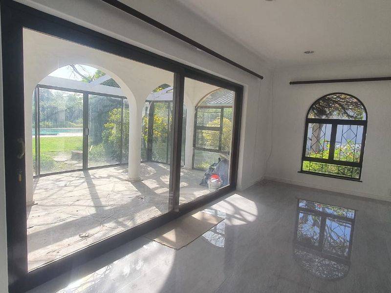Spacious living area featuring large sliding glass doors, arched windows with security bars, and polished tiled flooring, offering direct access to the patio.