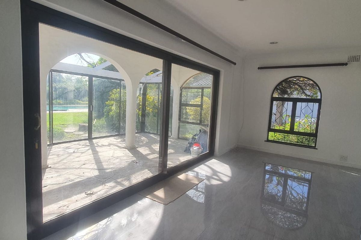 Spacious living area featuring large sliding glass doors, arched windows with security bars, and polished tiled flooring, offering direct access to the patio.