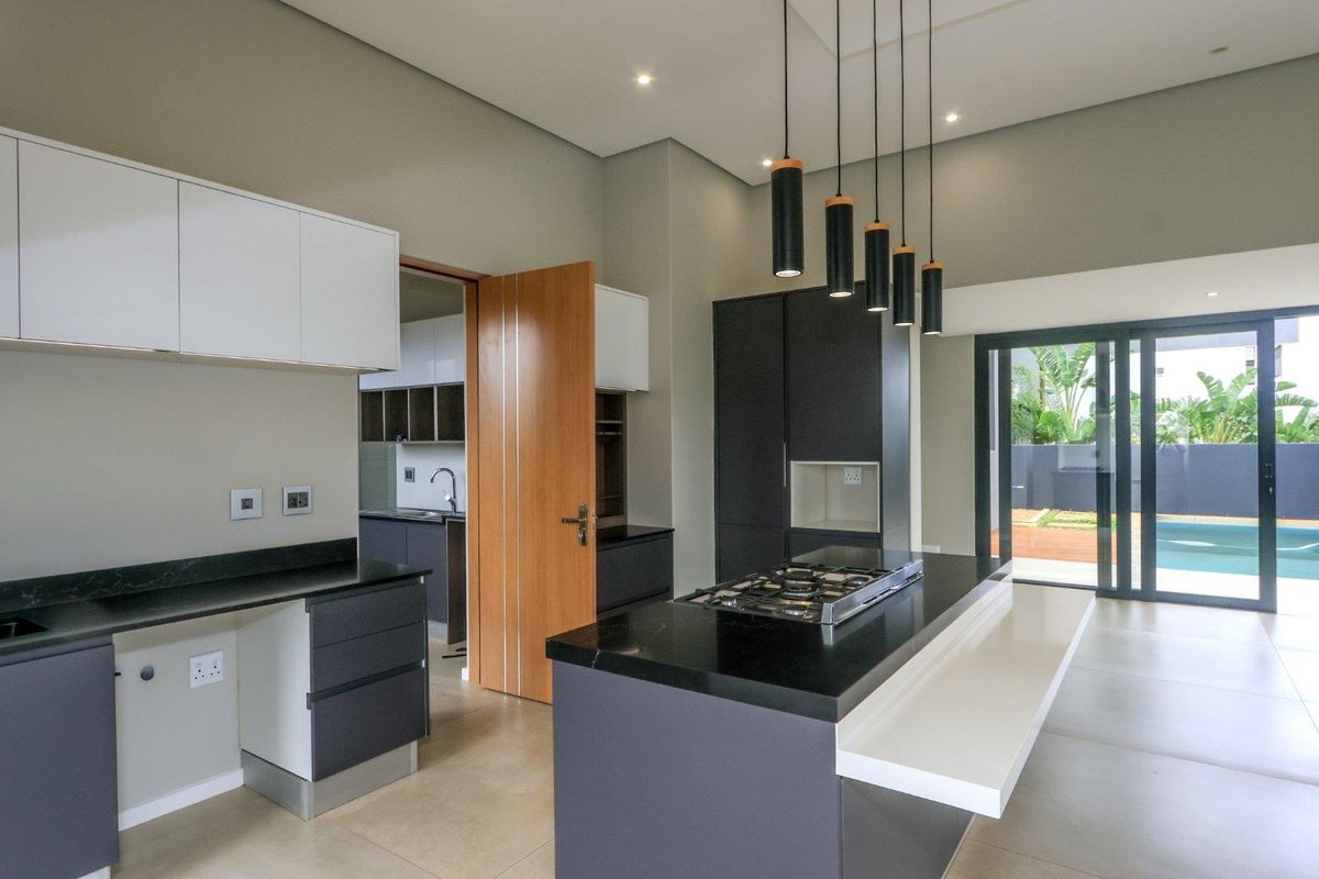 Modern open-plan kitchen featuring a central island with gas cooktop, sleek cabinetry, stone countertops, and direct access to the outdoor pool area.
