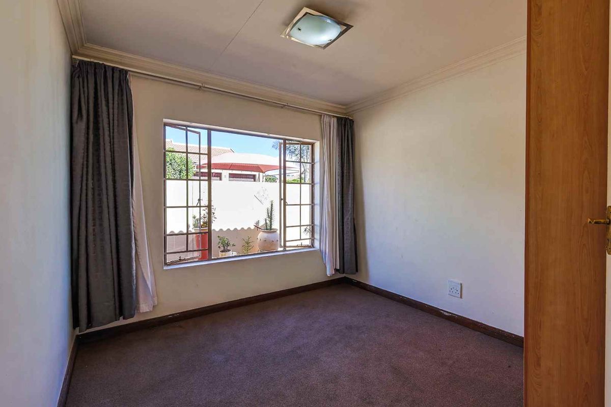 A vacant bedroom featuring carpeted flooring, a large window with metal frames, and crown molding, offering a neutral space ready for personalization.