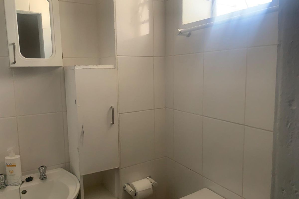 A compact bathroom featuring white wall tiles, a built-in vanity cabinet, a wall-mounted mirror cabinet, and a standard toilet.