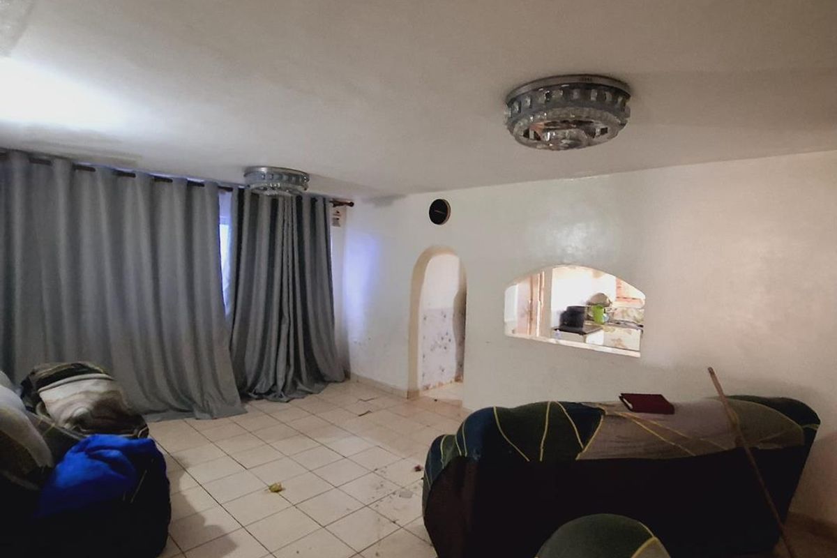Living room featuring tiled flooring, an arched doorway, and a pass-through window to the kitchen area, requiring significant cosmetic updates and repairs.