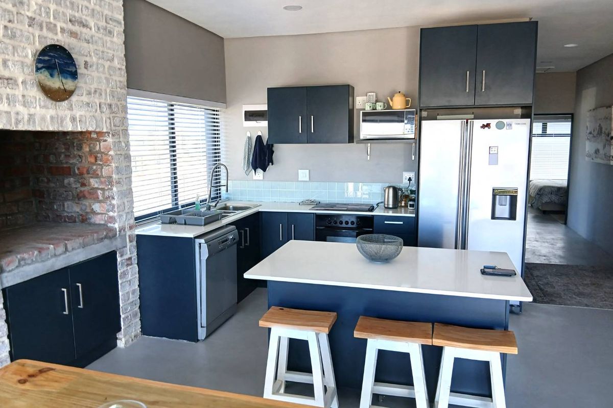 Modern kitchen featuring dark cabinetry, stone countertops, a central island with breakfast bar, and an integrated brick fireplace feature.