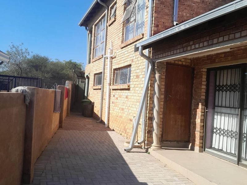 A side view of the property featuring a face brick facade, paved walkway, and a sliding door entrance with security gate.